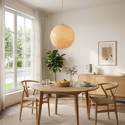 A modern spherical swirl glass pendant light hangs above a wooden dining table in a bright, contemporary room with natural decor and large windows.