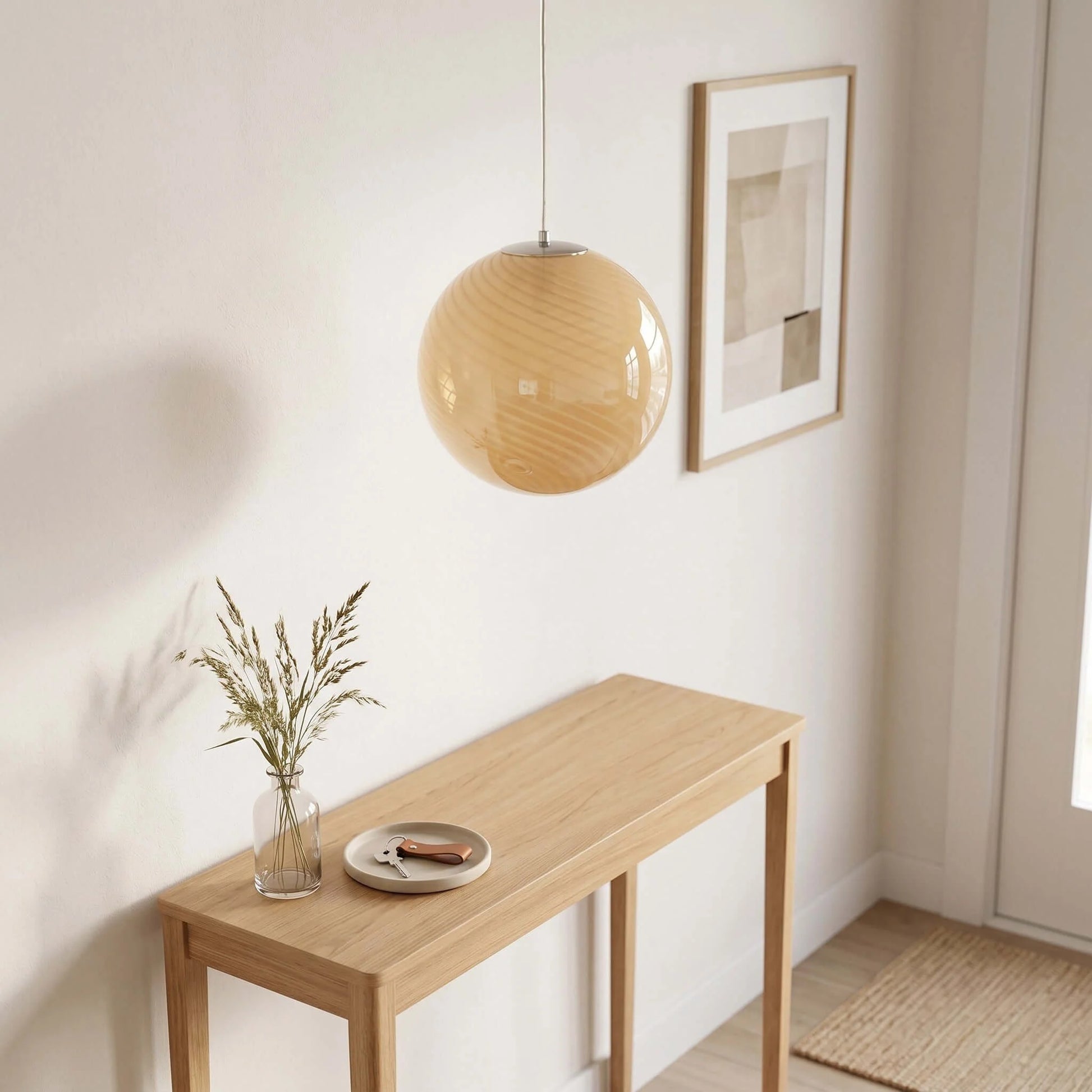 A modern spherical glass pendant light with a subtle swirl pattern, hanging above a light oak console table in a minimalist hallway interior.