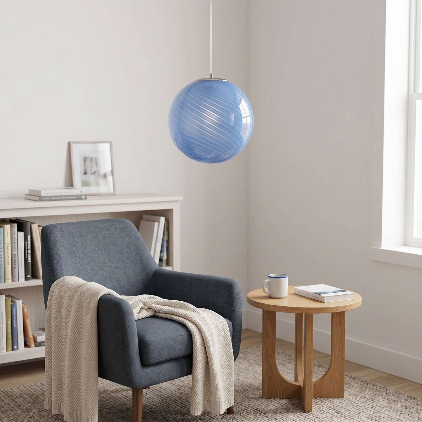 A modern blue swirl glass pendant light hangs above a cosy reading nook featuring a dark blue armchair, a cream throw, and a small wooden side table.