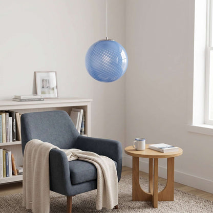 A modern blue swirl glass pendant light hangs above a cosy reading nook featuring a dark blue armchair, a cream throw, and a small wooden side table.
