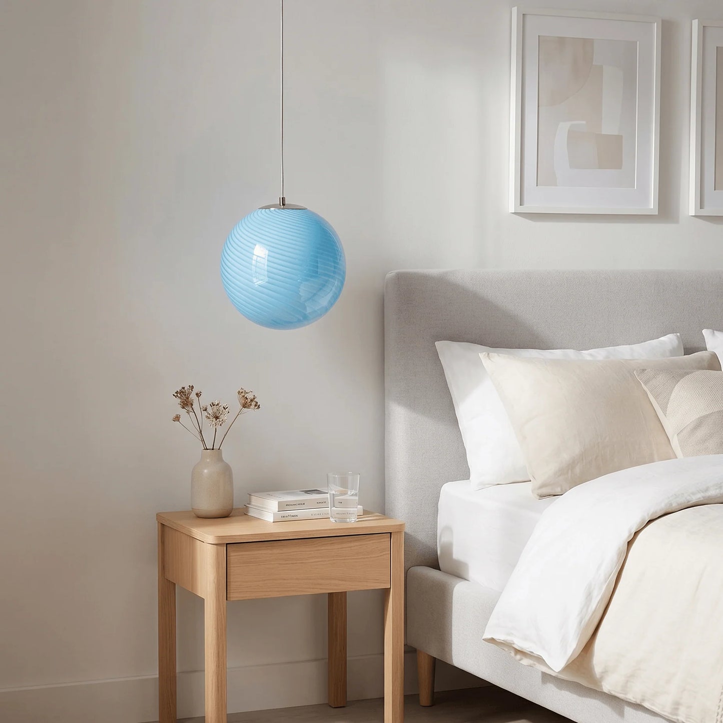 A light blue swirl glass pendant light hanging above a wooden bedside table in a modern bedroom with a grey upholstered headboard and neutral bedding.