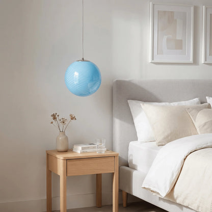 A light blue swirl glass pendant light hanging above a wooden bedside table in a modern bedroom with a grey upholstered headboard and neutral bedding.
