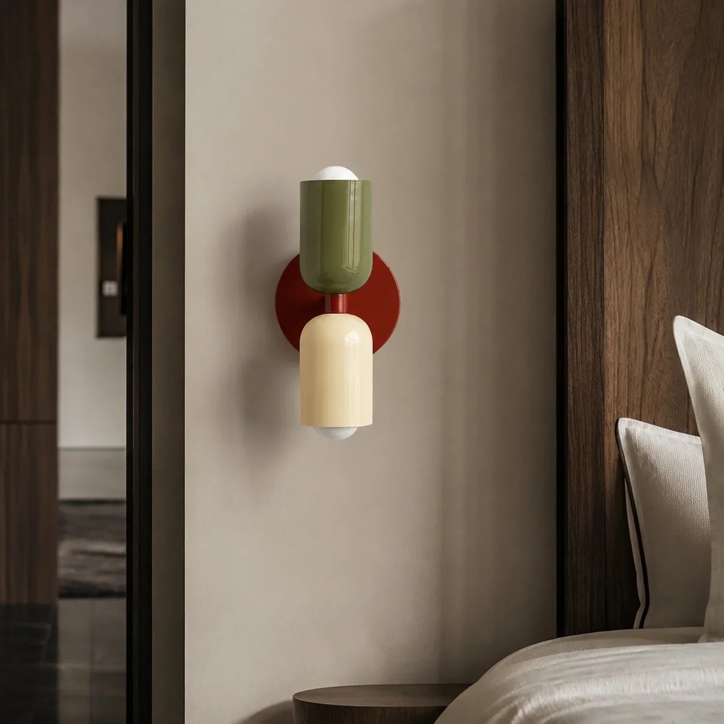 Contemporary dual-cylinder wall lamp featuring a red wine circular base with green and cream cylindrical shades mounted on a neutral bedroom wall.