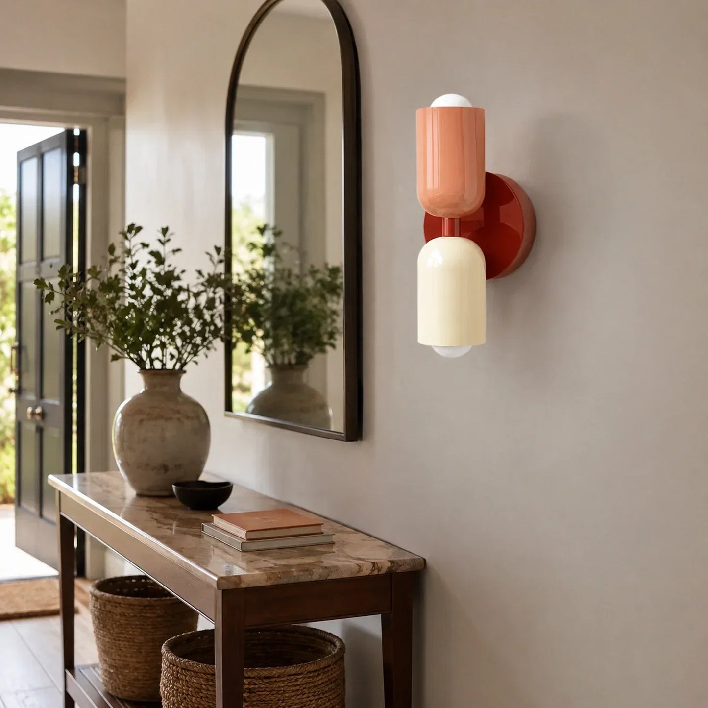 Contemporary dual-cylinder wall lamp in red wine, cream and terracotta tones mounted on a hallway wall above a marble console table and arched mirror.