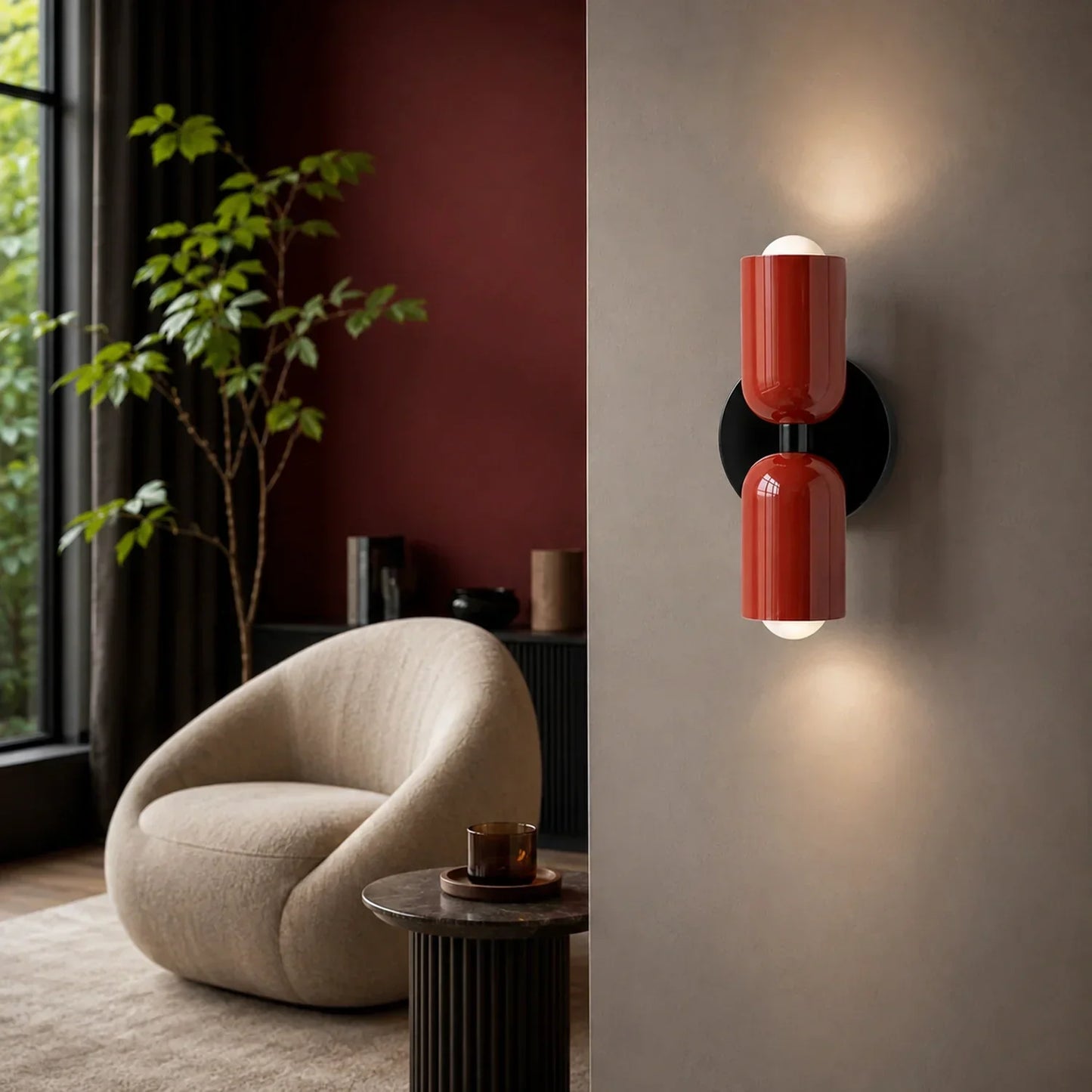 Glossy red dual-cylinder wall lamp mounted on a neutral wall, casting a warm up and down light in a contemporary living room with a cream armchair.
