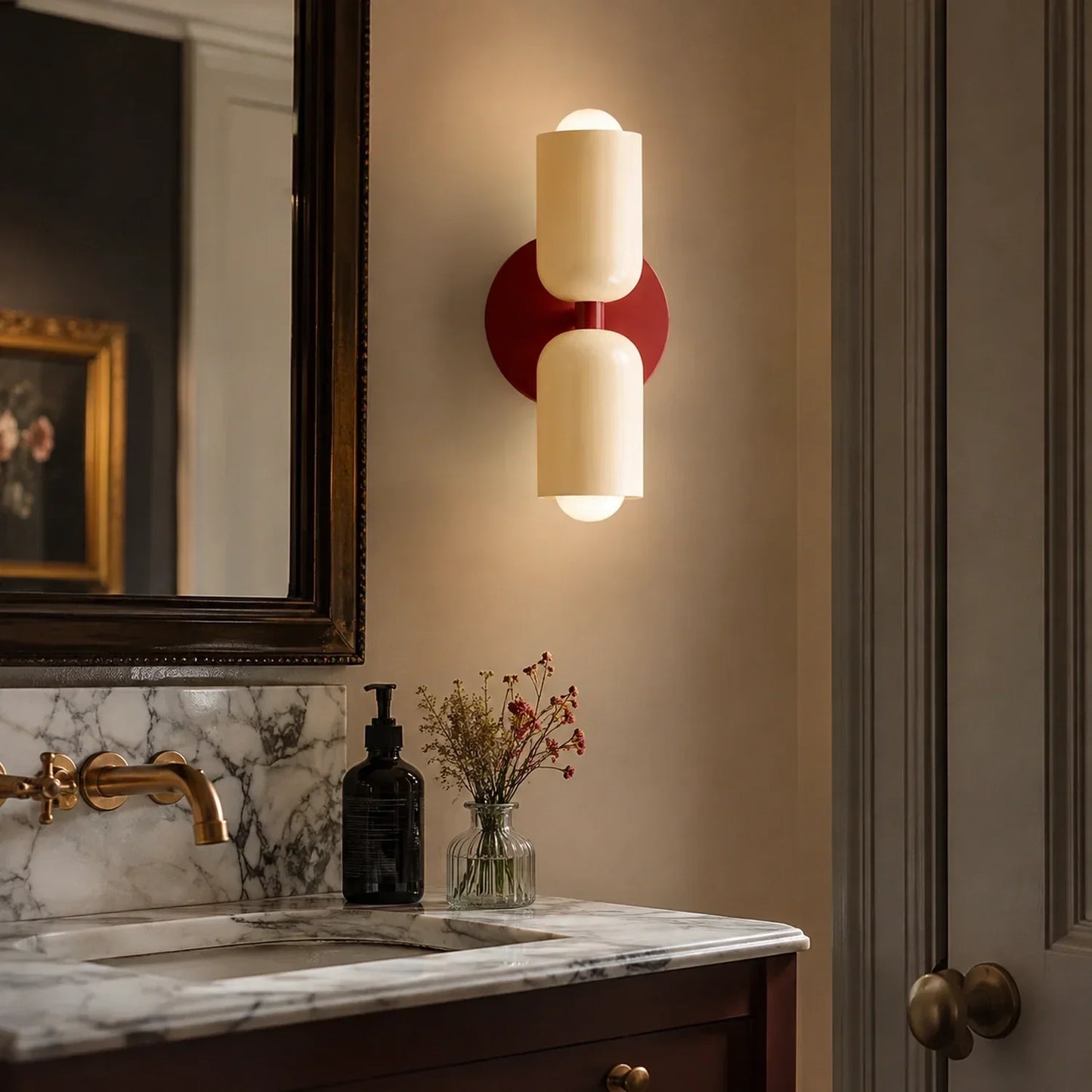 Contemporary red wine dual-cylinder metal wall lamp mounted above a marble bathroom vanity, providing warm up and down lighting in a modern interior.
