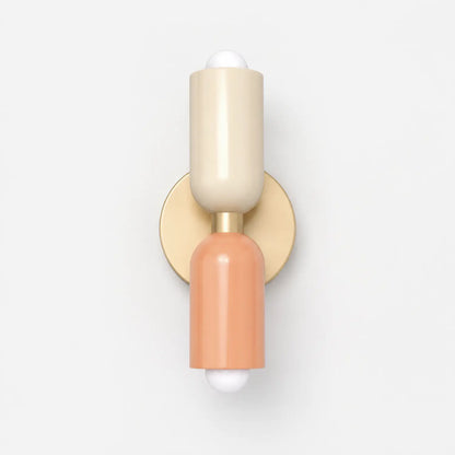 Contemporary dual-cylinder wall lamp featuring a cream and peach finish with a circular gold mounting plate, designed for up and down lighting.