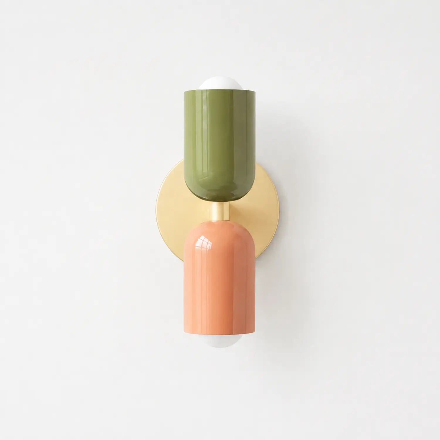 Contemporary dual-cylinder wall lamp featuring a circular gold backplate with one olive green and one terracotta orange cylindrical light fixture.