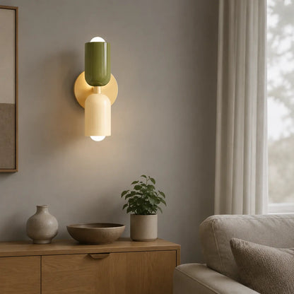 Contemporary dual-cylinder wall lamp with green and cream shades mounted on a grey wall above a wooden sideboard in a modern living room interior.