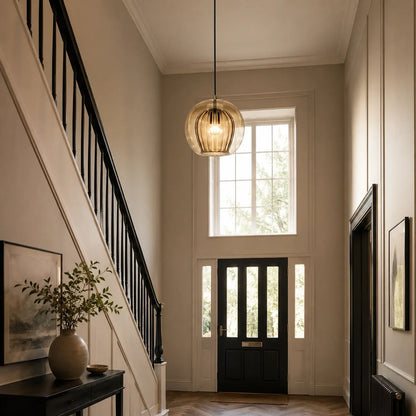 A 25cm amber ribbed glass globe pendant light hanging in a bright, modern hallway with a black staircase and front door, emitting a cool white glow.