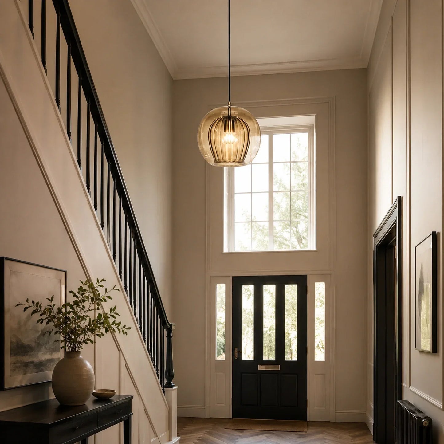 A 25cm amber ribbed glass globe pendant light suspended in a bright, modern hallway with a staircase and black front door, creating a warm atmosphere.