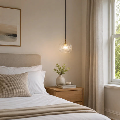 A 15cm clear ribbed glass globe pendant light hanging above a bedside table in a modern, neutrally decorated bedroom with soft ambient lighting.