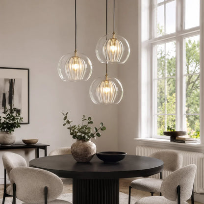 Three contemporary ribbed glass globe pendant lights hanging above a round black dining table in a bright, modern dining room with large windows.
