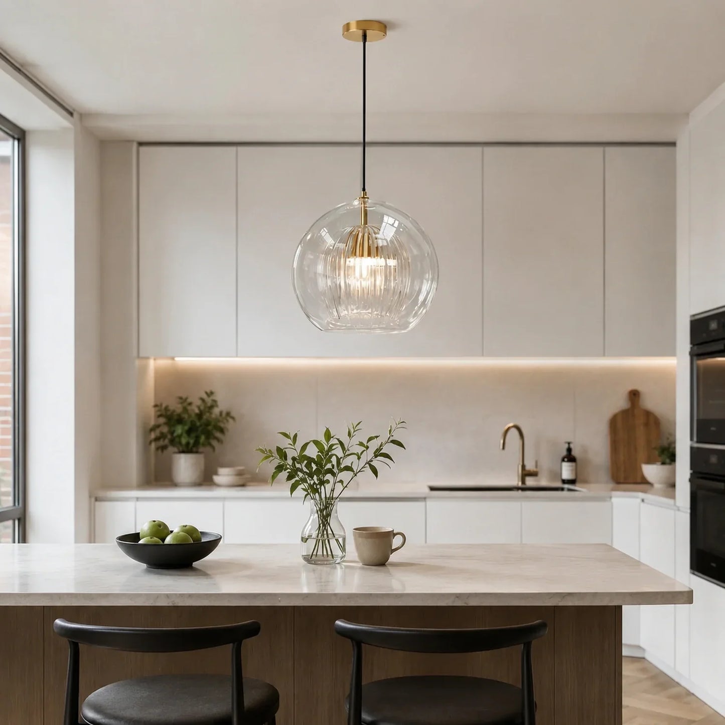 Contemporary ribbed glass globe pendant light with brass detailing hanging above a modern kitchen island with marble worktop and black bar stools.