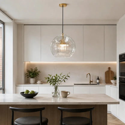 Contemporary ribbed glass globe pendant light with brass detailing hanging above a modern kitchen island with marble worktop and black bar stools.