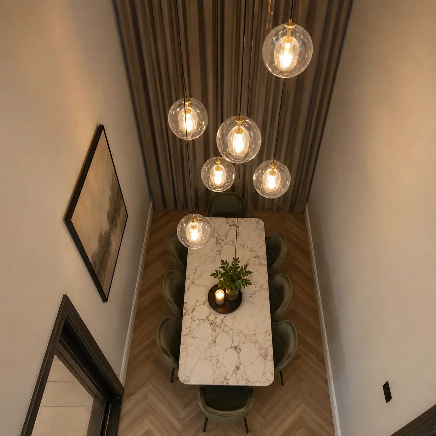 A cluster of contemporary ribbed glass globe pendant lights hanging above a marble dining table with green velvet chairs in a modern dining room setting.