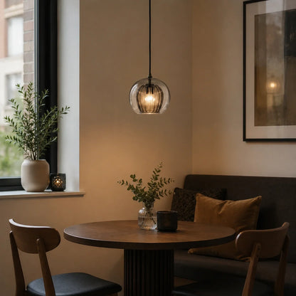 A 20cm smoky grey ribbed glass globe pendant light hangs above a small wooden dining table in a cosy, modern kitchen setting with soft ambient lighting.
