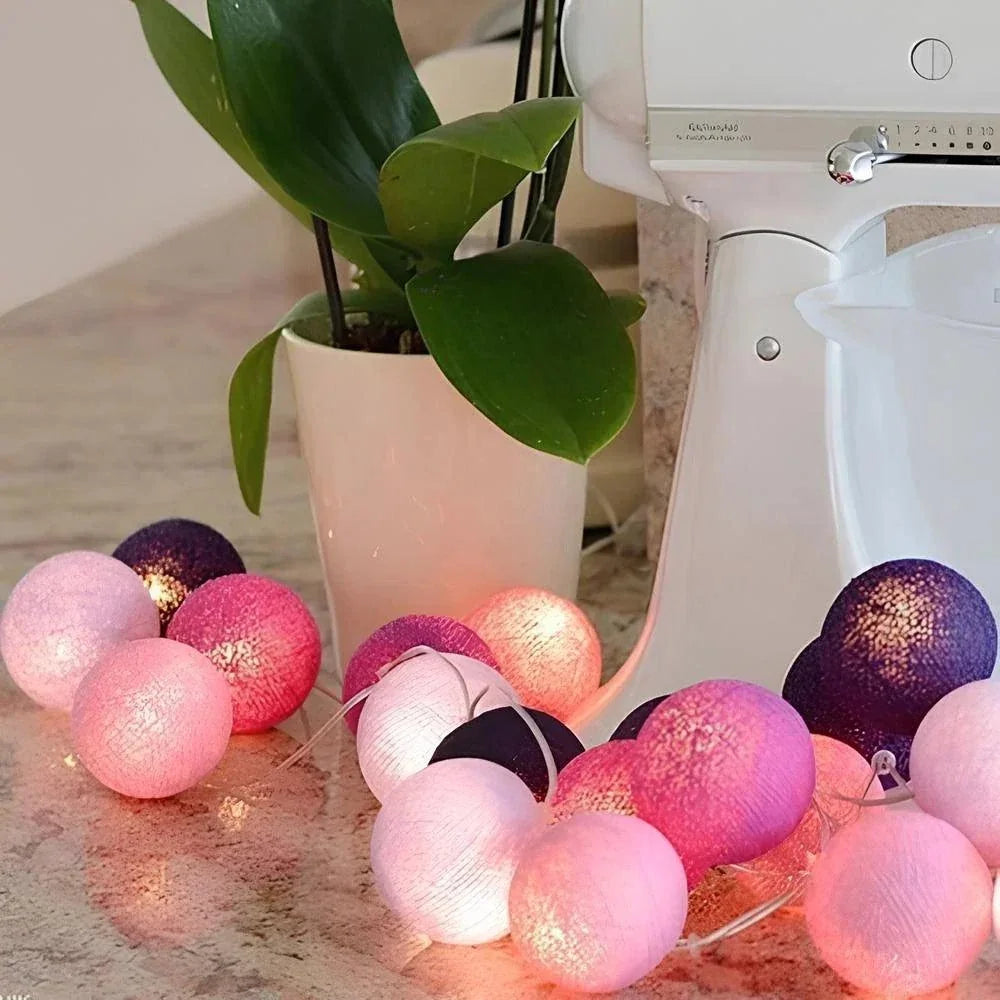 Pink and purple cotton ball garland beside a plant