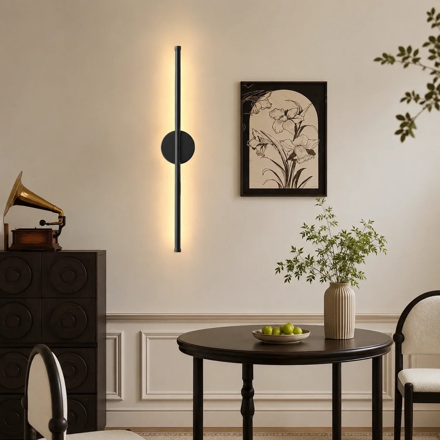 Modern black dimmable LED wall light mounted vertically in a stylish dining room, casting a warm glow on the wall above a dark wooden table and chairs.