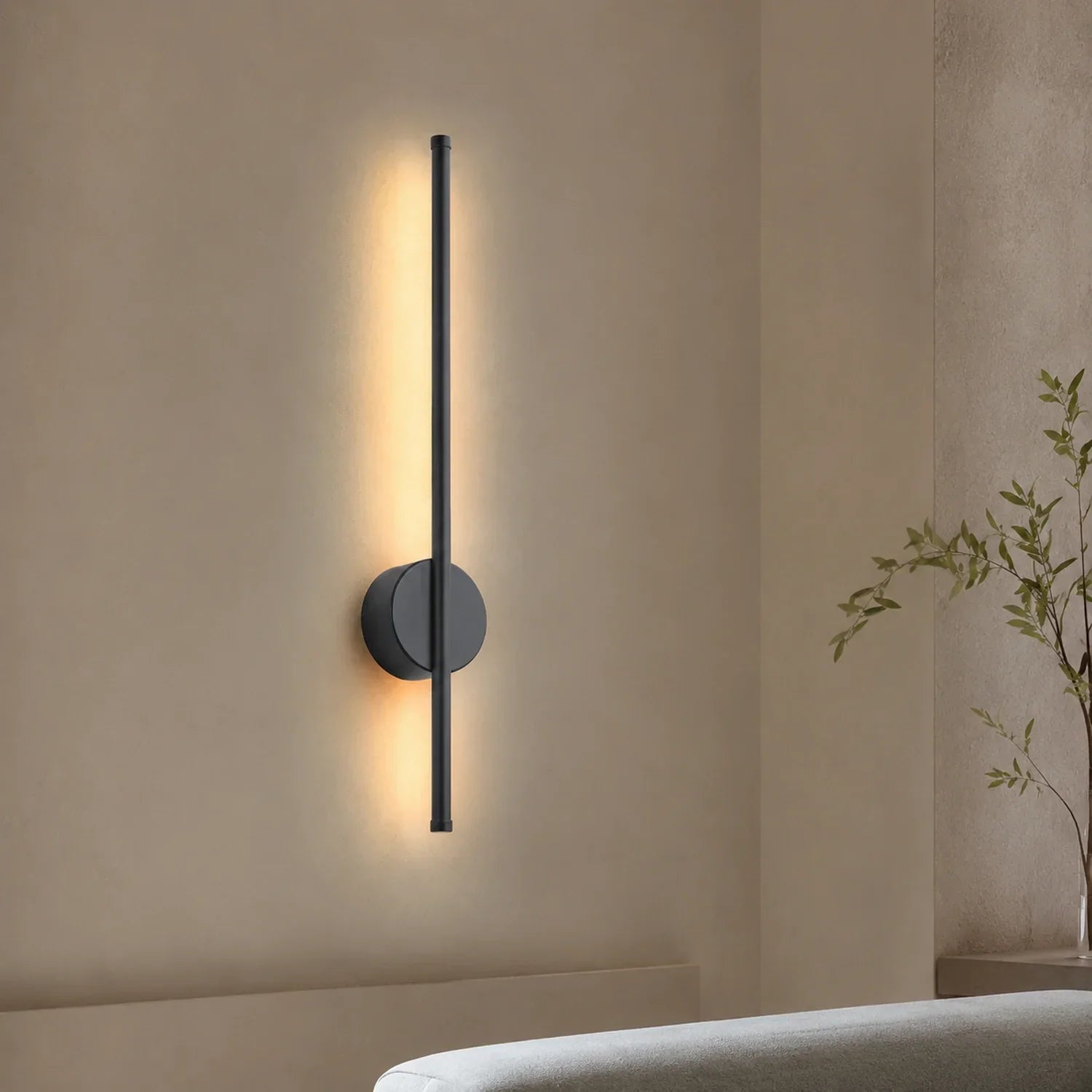 A modern, slimline black LED wall light mounted vertically, emitting a warm, soft glow against a neutral bedroom wall for elegant ambient lighting.