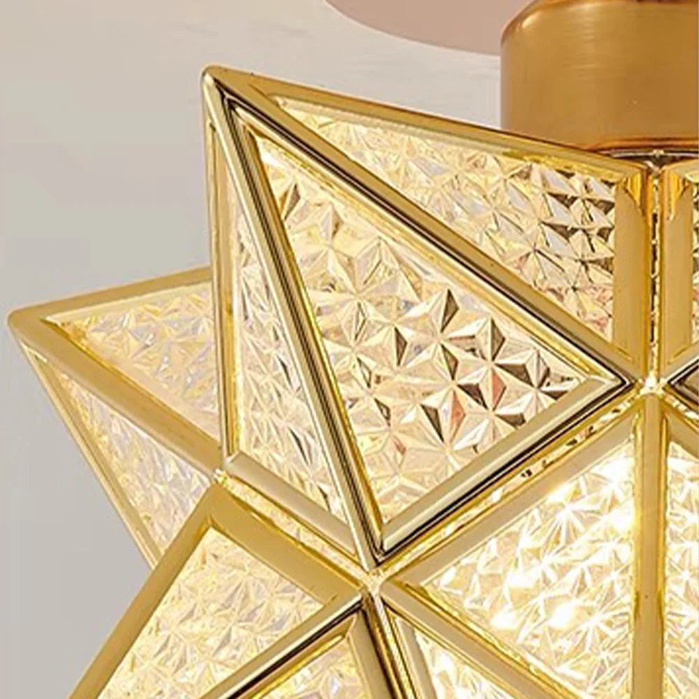 Close-up of a five-pointed star flush mount ceiling light featuring a gold metal frame and textured, geometric glass panels that diffuse warm light.