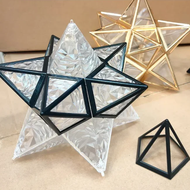 Geometric five-pointed star flush mount ceiling light with a black iron frame and textured glass panels, displayed alongside gold and pyramid accents.