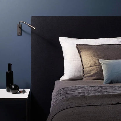 A flexible LED reading wall lamp mounted above a dark upholstered headboard in a modern bedroom, providing focused light for bedside reading.