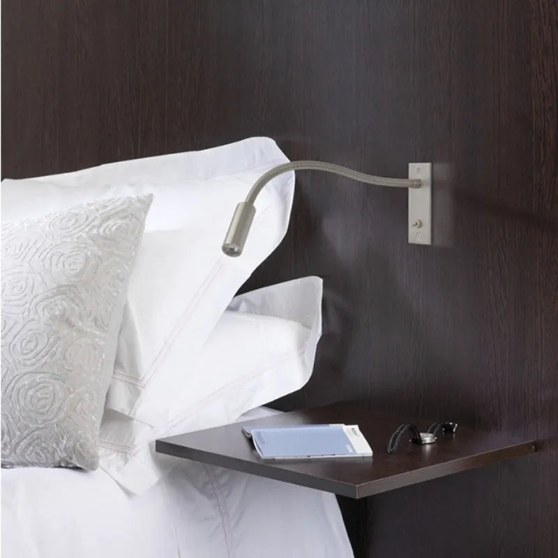 Flexible LED reading wall lamp mounted above a dark wood bedside table with white pillows, providing adjustable task lighting for the bedroom.