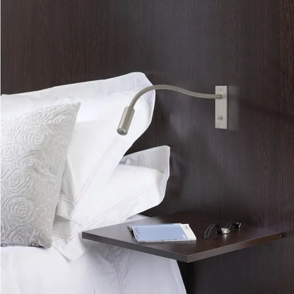 Flexible LED reading wall lamp mounted above a dark wood bedside table with white pillows, providing adjustable task lighting for the bedroom.