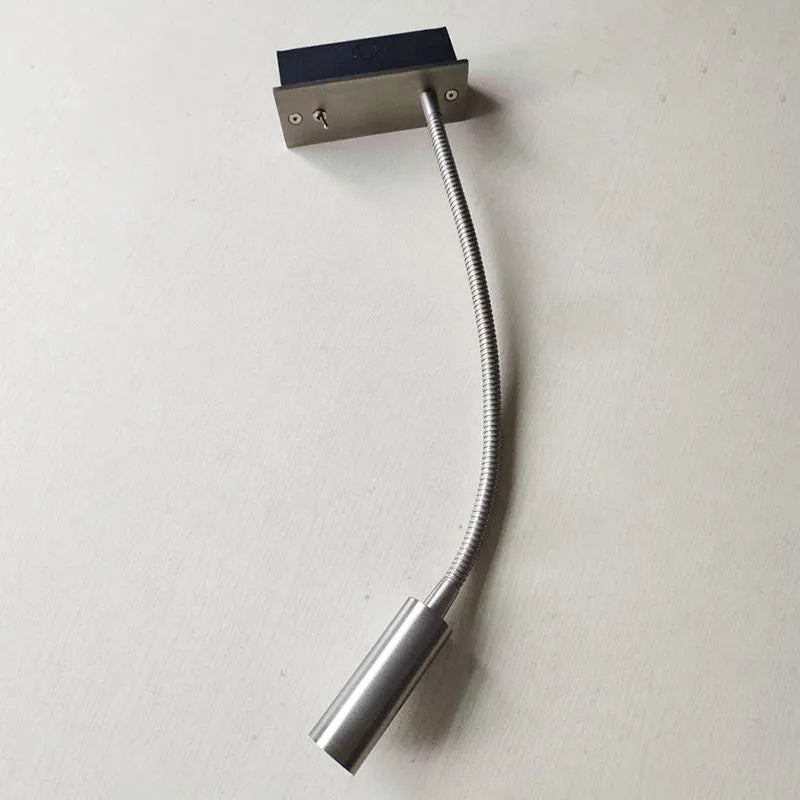 A flexible LED reading wall lamp in a brushed silver finish, featuring a flexible gooseneck arm, a cylindrical light head, and a toggle switch.