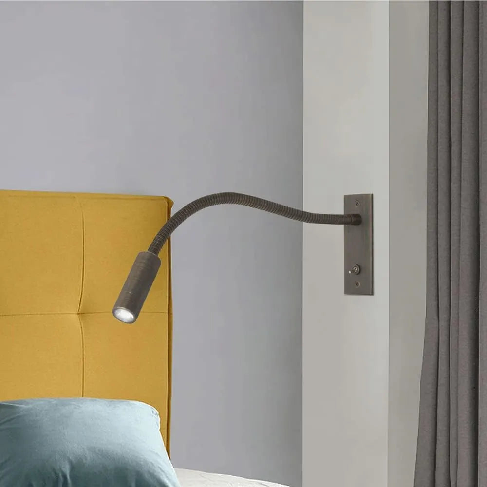 A flexible LED reading wall lamp with a dark metal gooseneck arm, mounted on a wall beside a yellow headboard to provide focused bedside lighting.