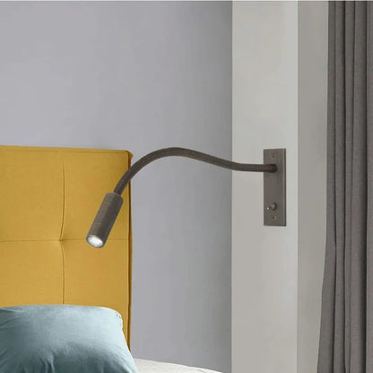 A flexible LED reading wall lamp with a dark metal gooseneck arm, mounted on a wall beside a yellow headboard to provide focused bedside lighting.