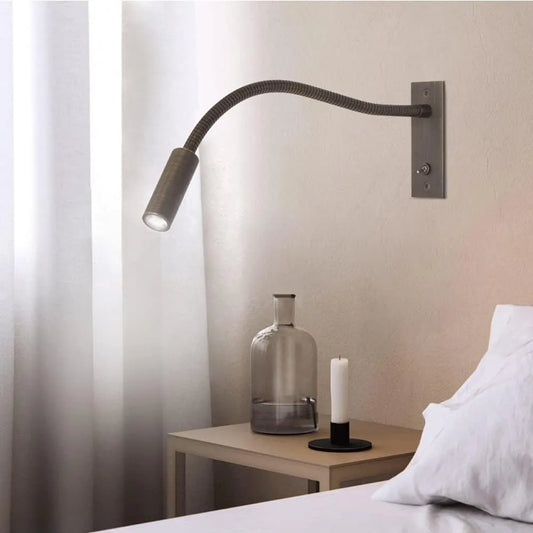 Flexible LED reading wall lamp with a metallic finish mounted above a bedside table, featuring an adjustable neck and a toggle switch for easy control.