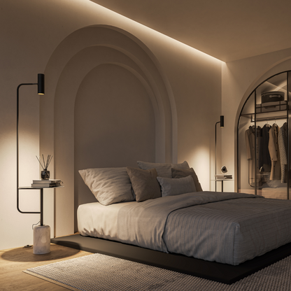 Black floor lamp with table beside a bed in low light