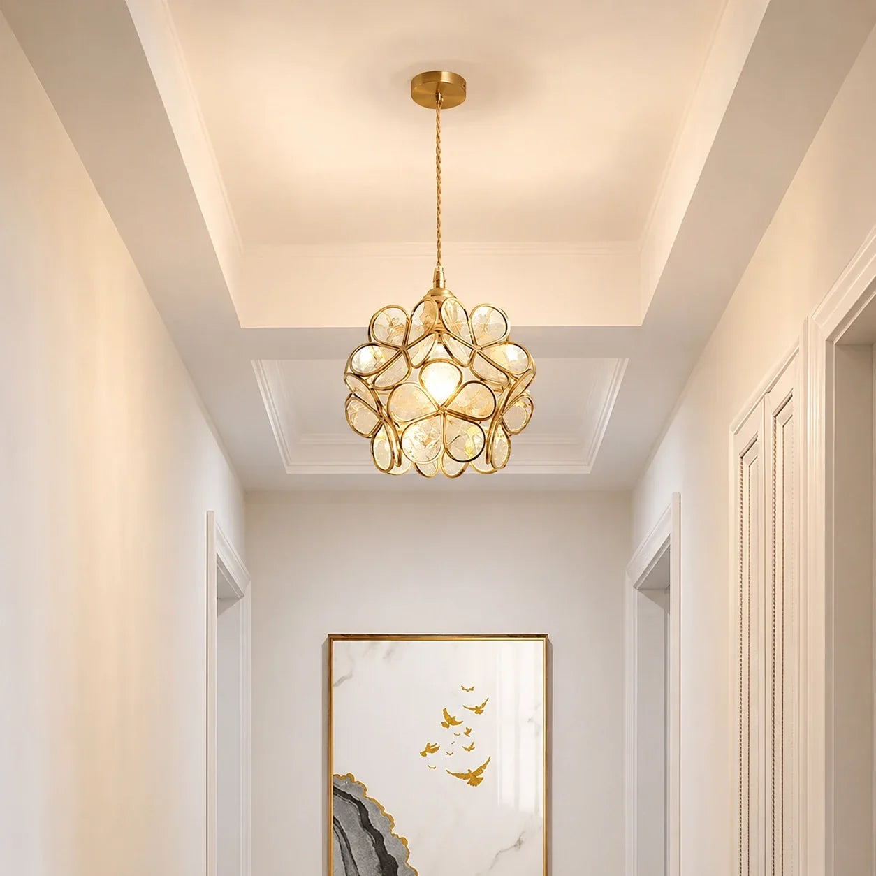Floral glass petal pendant light with a warm metallic finish, suspended in a bright hallway above a framed piece of wall art.