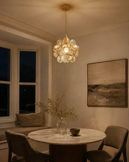 Floral glass petal pendant light with a warm glow, suspended above a marble dining table in a cosy, stylishly decorated room with a window seat.