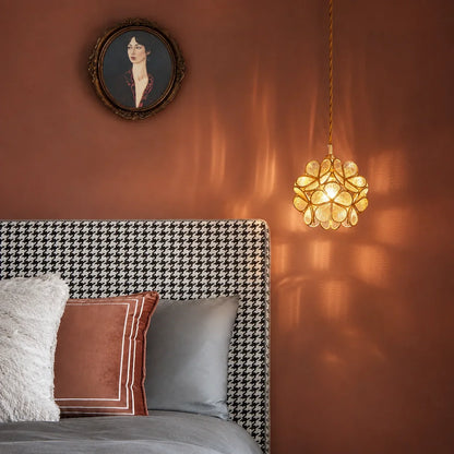 Floral glass petal pendant light with a warm glow hanging above a houndstooth headboard in a bedroom with terracotta walls and vintage wall art.