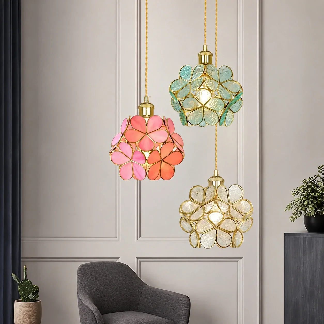 Three floral glass petal pendant lights in pink, teal and clear glass with gold fixtures hanging in a modern living room interior.