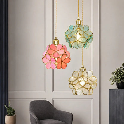Three floral glass petal pendant lights in pink, teal and clear glass with gold fixtures hanging in a modern living room interior.