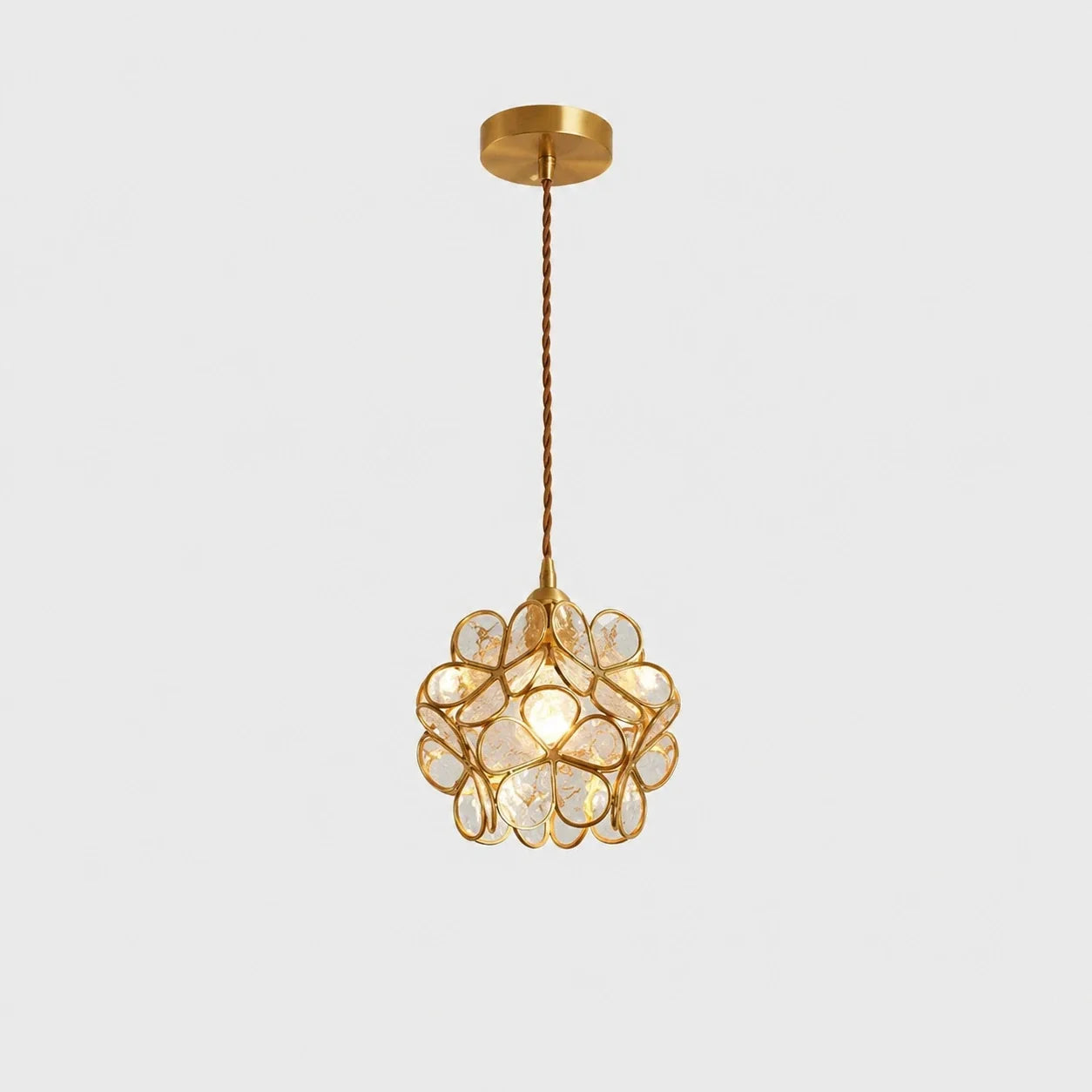 Floral glass petal pendant light in transparent A finish with a warm glowing bulb, suspended by a twisted cable from a circular copper ceiling rose.