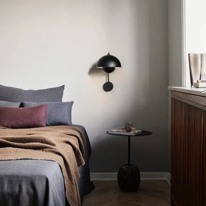 Black Flowerpot-style wall lamp beside a bed