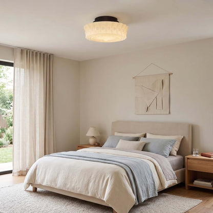 French vintage flushmount ceiling light with a textured glass shade installed in a neutral, modern bedroom with a made bed and linen curtains.