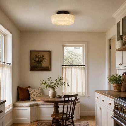 French vintage flushmount ceiling fixture with a textured glass shade installed in a cosy, traditional kitchen breakfast nook with wooden furniture.