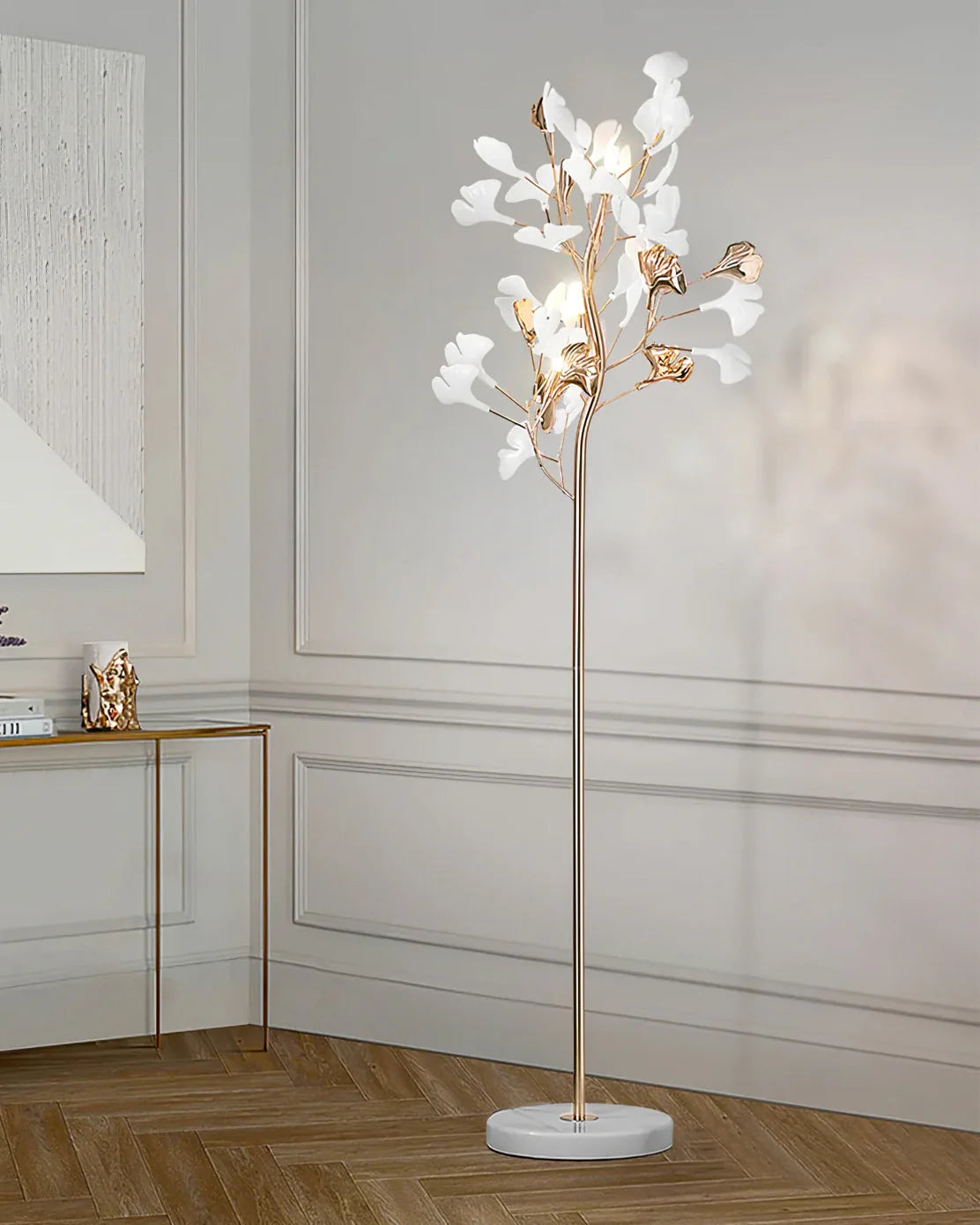 An elegant gold-coloured ginkgo leaf LED floor lamp with white and gold leaf details and a marble base, standing in a modern panelled living room.