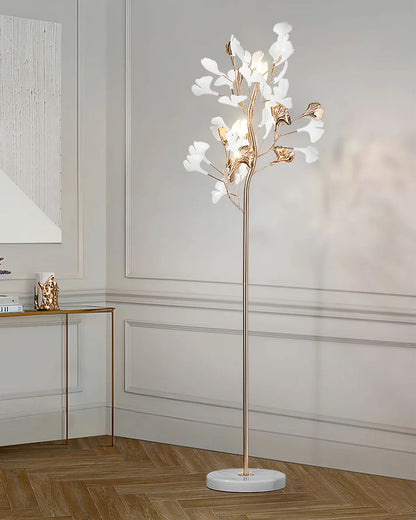 An elegant gold-coloured ginkgo leaf LED floor lamp with white and gold leaf details and a marble base, standing in a modern panelled living room.