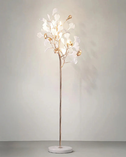 A gold Ginkgo Leaf LED floor lamp with five glowing lights and white leaf-shaped shades, standing on a round white marble base against a plain wall.