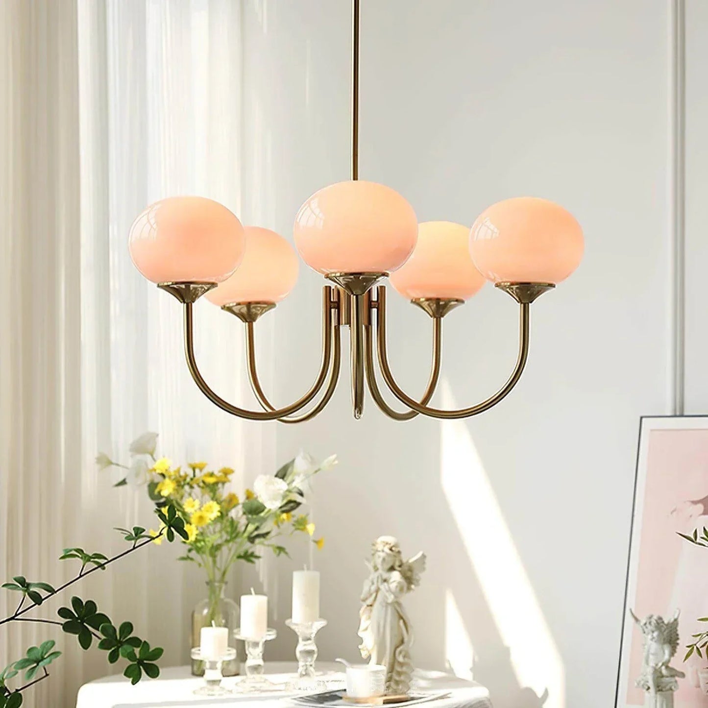 Modern glass ball pendant light with five curved brass arms and peach-coloured glass globes, hanging in a bright, stylish interior setting.
