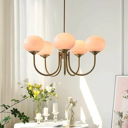 Modern glass ball pendant light with five curved brass arms and peach-coloured glass globes, hanging in a bright, stylish interior setting.