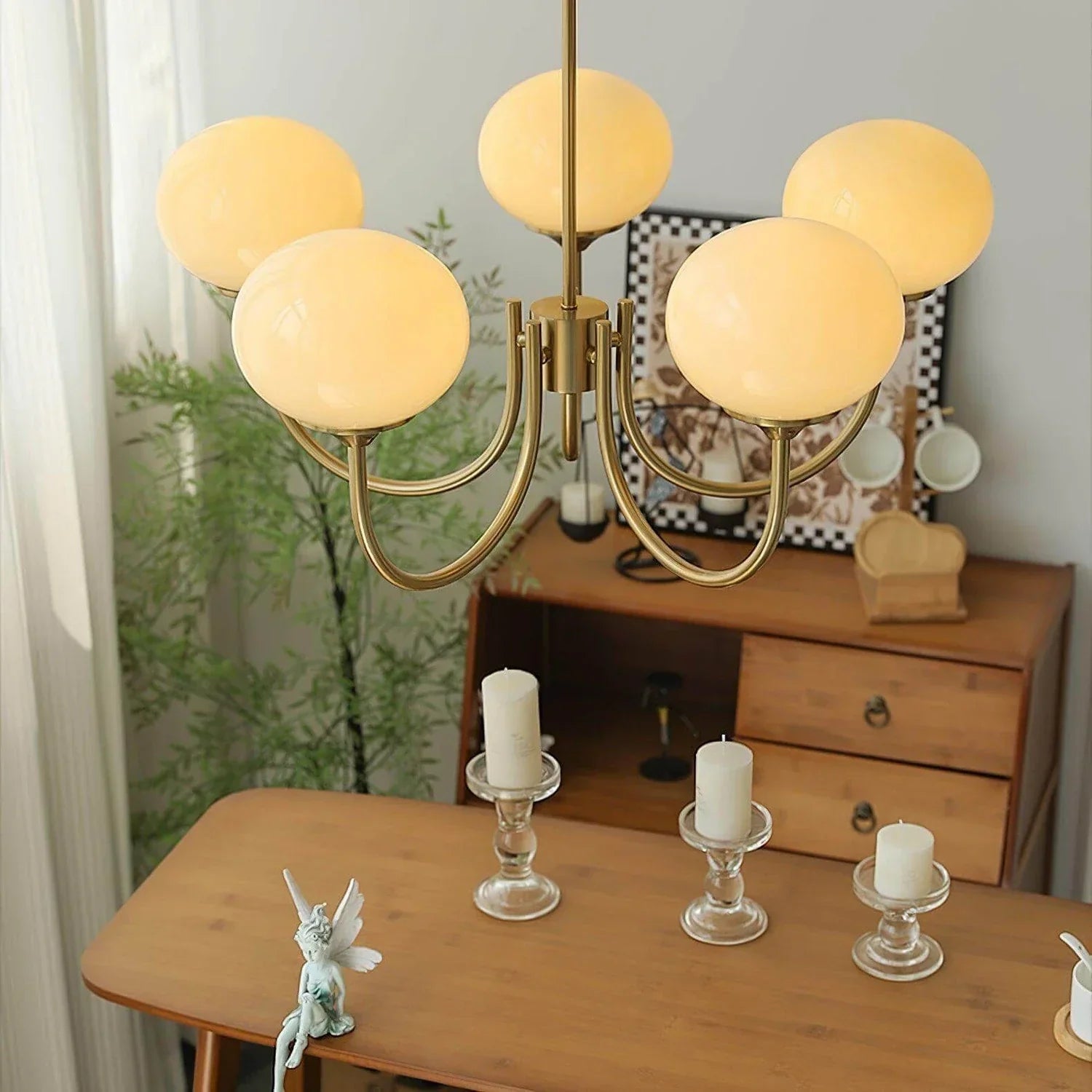 Modern five-light pendant ceiling fixture featuring glowing frosted glass ball globes on a curved brass metal frame, hanging above a wooden table.