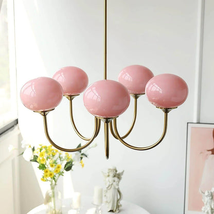 Modern five-light pendant ceiling fixture with curved brass arms and glossy pink glass ball shades, hanging in a bright interior.